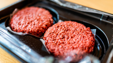 Closeup of two raw uncooked red vegan meat burger patties in plastic packaging