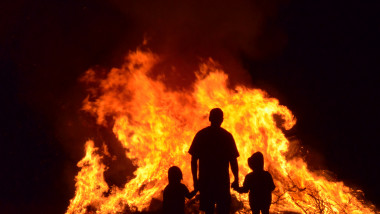 Man and children in silhouette watching the flames of a huge bonfire.