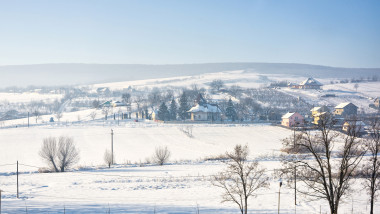 Winter landscape of romania village with snow, near Iasi city, church and houses, blue sky