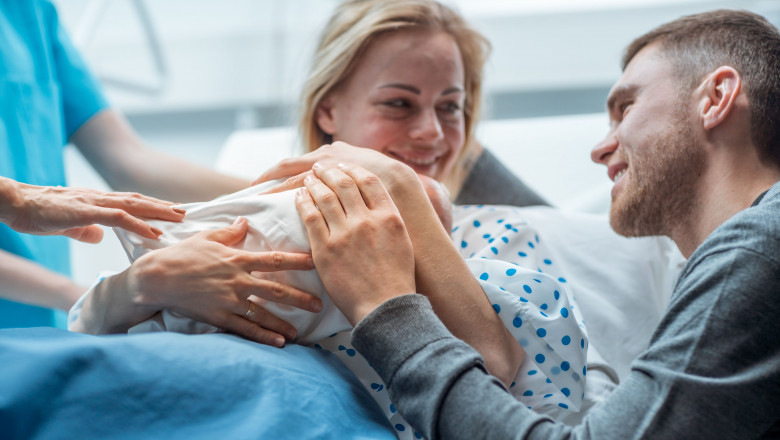 In the Hospital Midwife Gives Newborn Baby to a Mother to Hold, Supportive Father Lovingly Hugging Baby and Wife. Happy Family in the Modern Delivery Ward.