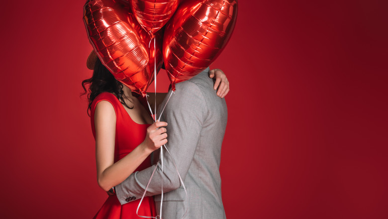 couple covering faces with bundle of balloons isolated on red