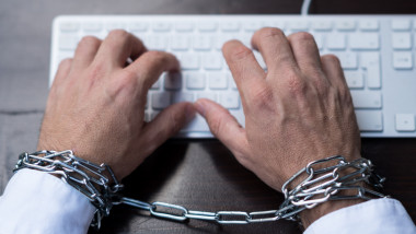 Businessman hands tied with chains on laptop keyboard