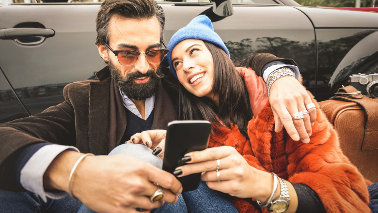 Hipster couple having fun with mobile smart phone at car roadtrip - Friendship concept with best friends connecting and sharing content on social media - Millennial generation as fashion influencer