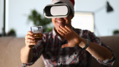 Bărbat poartă ochelari VR și cu un pahar de whisky