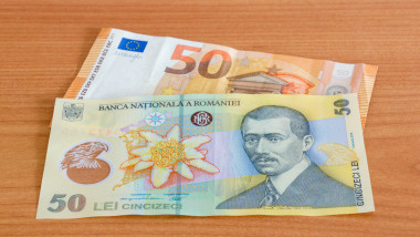 50 Euro banknote (EUR) and 50 Romanian lei banknote (RON) on wooden table.
