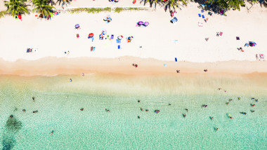 View from above, stunning aerial view of people sunbathing, swimming and relaxing on a beautiful tropical beach with white sand and turquoise clear water, Surin beach, Phuket, Thailand.