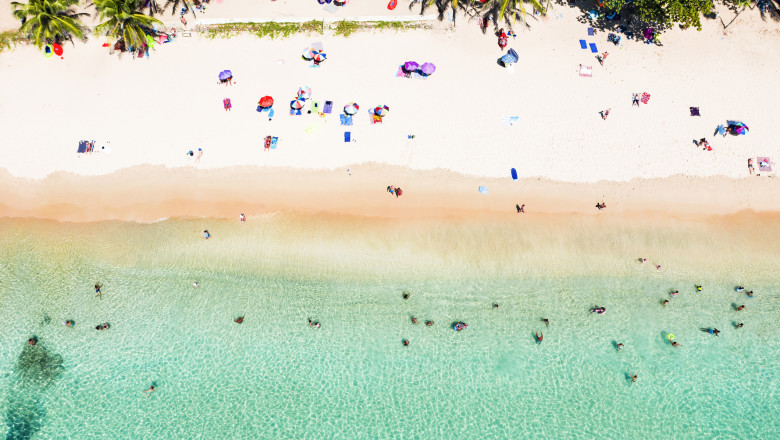 View from above, stunning aerial view of people sunbathing, swimming and relaxing on a beautiful tropical beach with white sand and turquoise clear water, Surin beach, Phuket, Thailand.