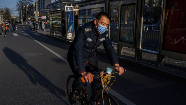 Un barbat cu masca se deplaseaza cu bicicleta pe strazile pustii dintr-un oras din China