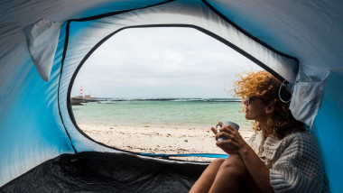 lonely beautiful woman sitting on the tent looking outside. wind on the hair and camping on the beach near the colors of water and shore. freedom and