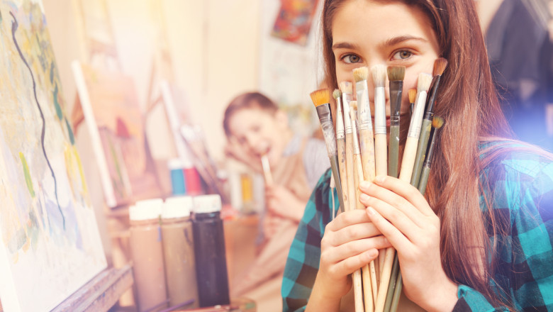 Beautiful girl holding bunch of messy painting brushes