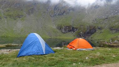 Travellers camping at a mountain lake in a misty landscape.