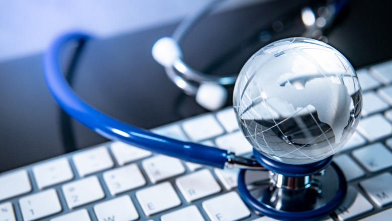 Global healthcare concept. World globe crystal glass on blue stethoscope on white keyboard. Health and medical science. Worldwide wellness business and technology