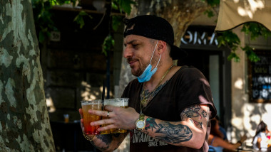 Bărbat din Italia, cu masca pe bărbie, ține în mâini pahare cu bere în perioada de relaxare a restricțiilor anti-Covid, după primul val al pandemiei.