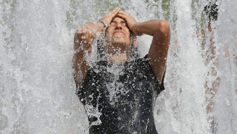 un barbat sta sub un jet de apa din cauza caldurii