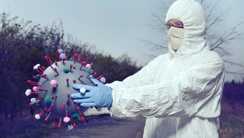 persoană îmbrăcată în costum de protecție ține un coronavirus în mâini