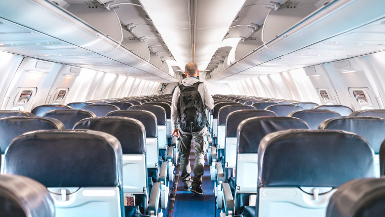 Un bărbat merge pe culoarul unui avion cu scaune goale