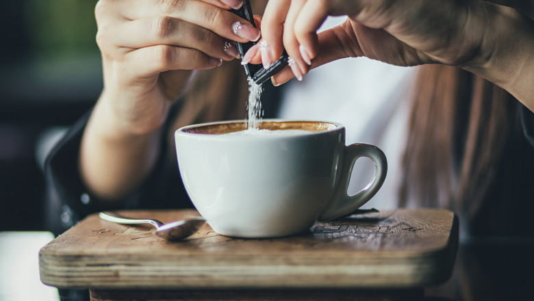femeie care isi pune un pliculet de zahar in cafea