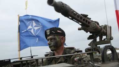 militar NATO cu o mitralieră și steagul NATO în fundal