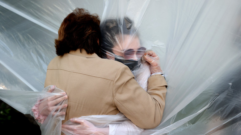 O femeie își îmbrățișează bunica printr-o folie de plastic, după luni de zile, la New York. Foto: GettyImages