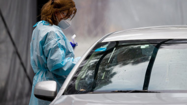 O asistentă medicală în echipament de protecție testează o persoană la Covid-19 dintr-o mașină.