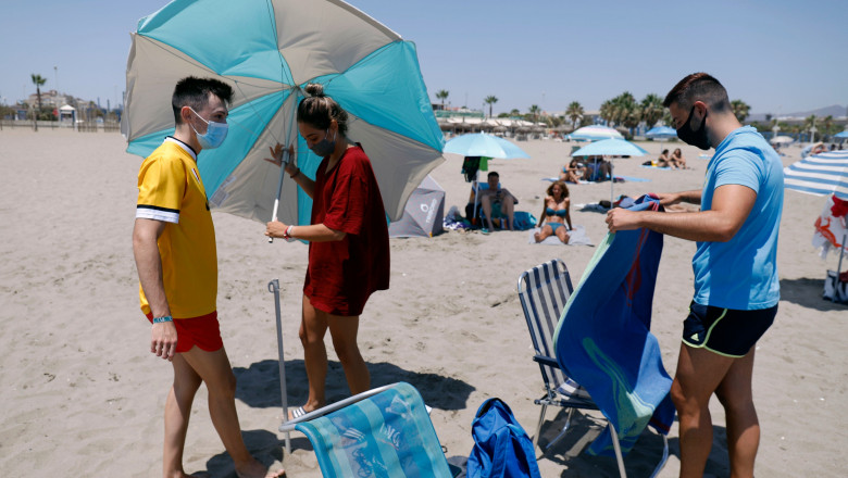 Tineri pe plaja din Malaga purtând măști de protecție