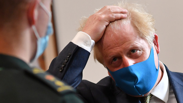 premierul britanic Boris Johnson îşi pune mâna în cap în timp ce poartă mască