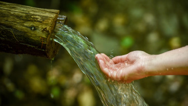 Image of drinking clean cold spring flowing water in nature during spring/summer time. Female hand is collecting the water for drinking. Close up shot with no recognizable face