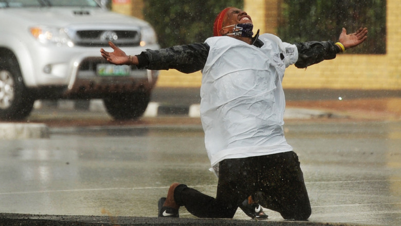 un cerșetor cade în genunchi și se bucură de ploaie în Cape Town, Africa de Sud, în timpul epidemiei de coronavirus
