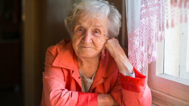 Elderly woman in red jacket sitting at the table in the house.