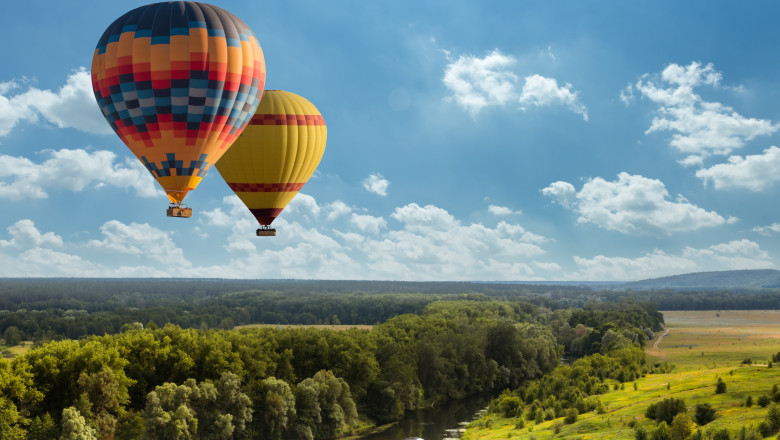 Colorful hot air balloon flying over green field and river