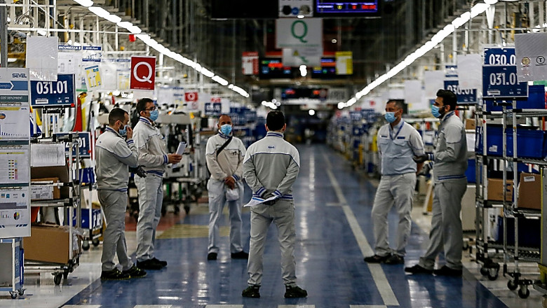 un grup de muncitori cu masti stau de vorba intr-o fabrica auto din Italia