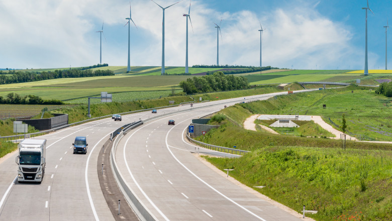 masini si camioane pe autostrada cu turbini eoliene pe fundal