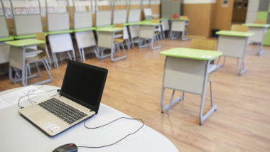 laptop pe masa profesorului in clasa cu scuane pregatite pentru elevi in timpul pandemiei
