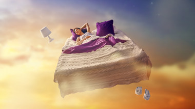 O tânără visează că zboară în timp ce doarme pe pat.