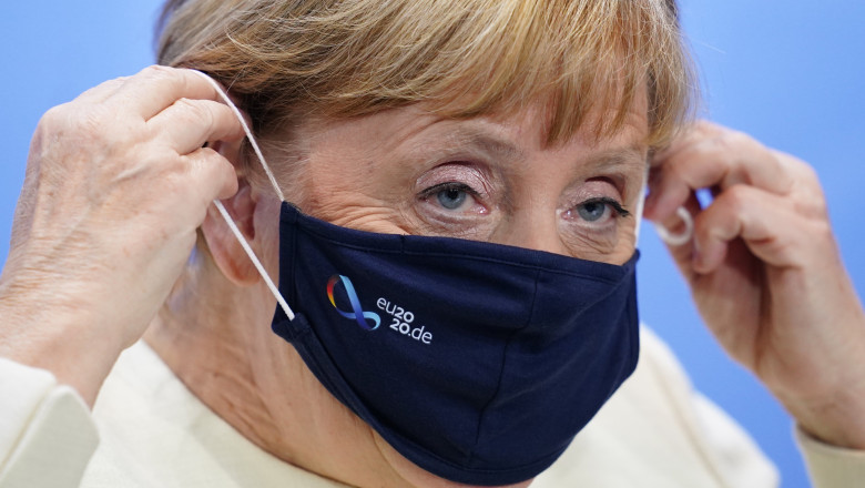 Angela Merkel își așază masca de protecție pe față.