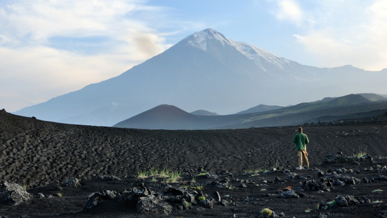 Un barbat sta in mijlocul unui camp, uitandu-se la vulcanul Tolbachik