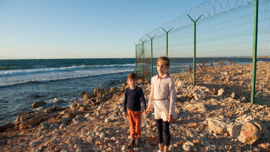 doi copii saraci stau langa un gard pe o plaja