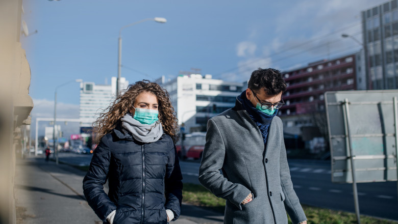 Doi tineri poartă masca de protecție pe stradă.