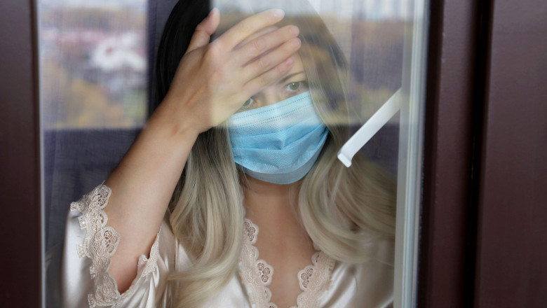 femeie cu masca in lockdown la fereastra casei