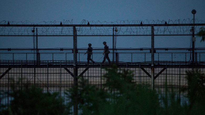 garn inalt cu sarma ghimpata si doi militari care patruleaza l frontiera dintre Coreea de Nord si Coreea de Sud