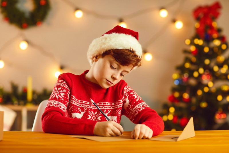 Băiat la masă scrie o scrisoare pentru Moş Crăciun