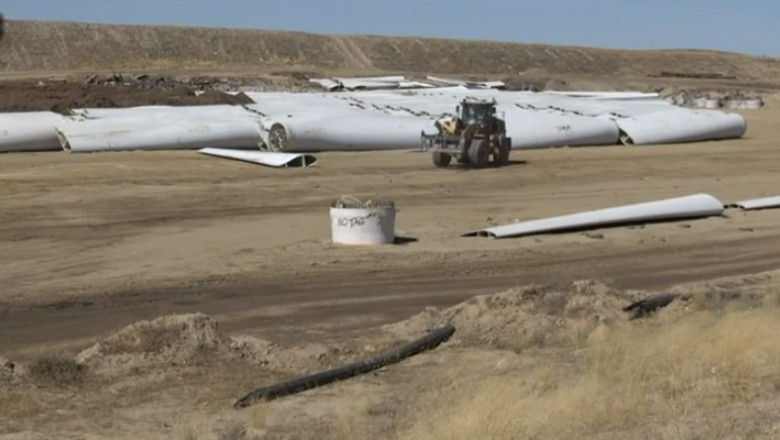 un buldozer lucreaza pe pamantul unde se afla pale uriase albe de turbine eoliene