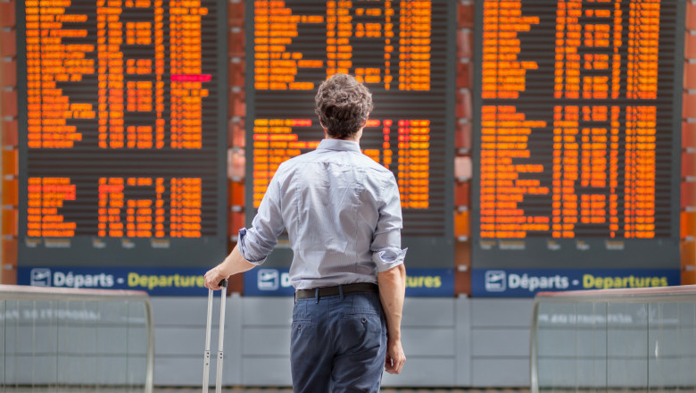 barbat cu bagaj pe aeroport se uita la o tabela de zboruri