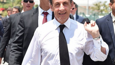 Nicolas Sarkozy in camasa si cravata, cu haina pe umar