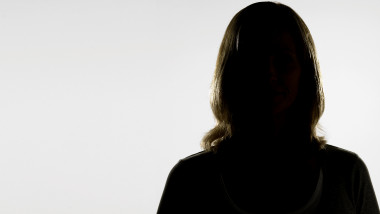 Mature woman standing in shadow against white background, portrait