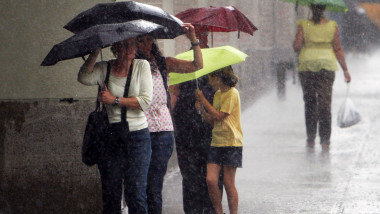 Oameni cu umbrele se feresc de ploaie