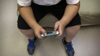 un copil cu obezitate se uita pe telefonul mobil
