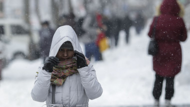 o femeie merge pe strada in bucuresti,cu gluga si manusi, pentru a se proteja de frig