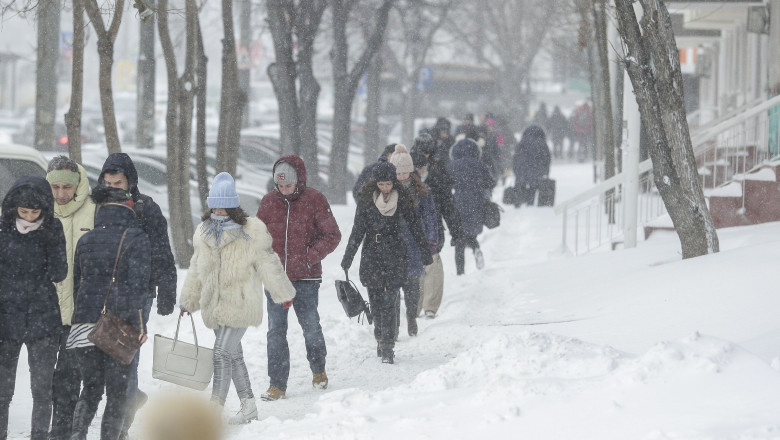 Oameni merg pe stradă pe cod galben de ninsoare