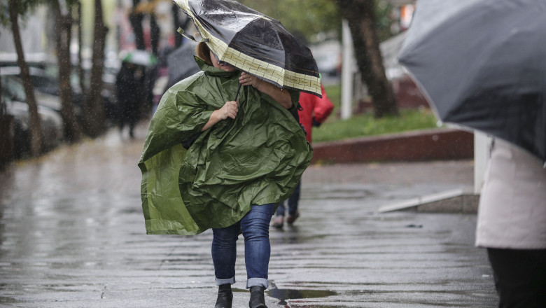 Femeie cu pelerină de ploaie și umbrelă pe vreme ploioasă